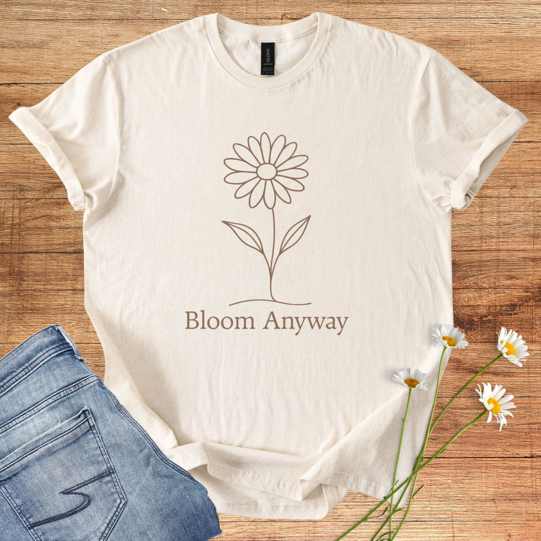 Natural t-shirt with a flower design and 'Bloom Anyway' text on a wooden surface with jeans and flowers.