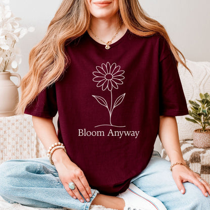 A person wearing a maroon t-shirt with a creamy off-white line-art flower graphic and 'Bloom Anyway' text underneath.