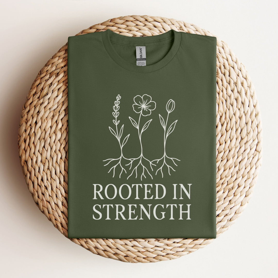 Green t-shirt with floral design and 'Rooted in Strength' text on a woven mat.